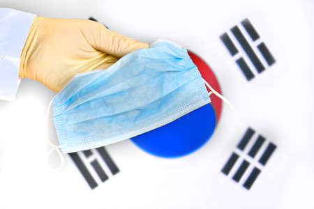 Protective mask in South Korea, concept coronavirus pandemic. Hand in a medical glove holds a mask to protect from the pandemic flu virus among Korean.の写真素材