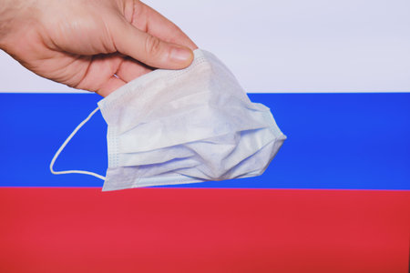 A hand holds a mask against the background of the Russian flag. Coronavirus control in the Russian...