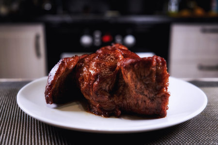 Big piece of meat on plate. Roast beef close-up. Barbecue meat in modern kitchen. Blurred background...