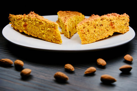 Pie on a big plate and almonds. Pieces of cake with nuts on a wooden dark background. Baking orange...