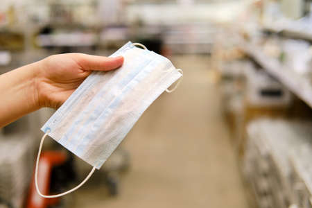 Hand in a medical glove holds a mask against viruses on the background of the shop, conceptの写真素材