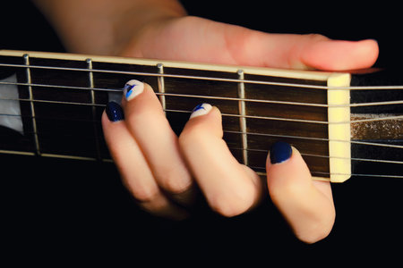 Female hand with manicure lying on the wooden neck of the guitar. Woman guitarist clamped a chord on...