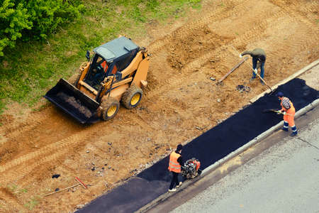 Road worker using a small bulldozer and workers with shovelsの写真素材