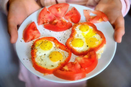 A woman holds a plate of quail eggs with tomato and bell pepperの写真素材