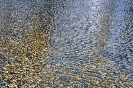 Background of transparent water, texture of ripples and waves on top of stones