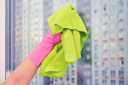 A gloved hand with a green cloth wipes a large window, close-upの写真素材