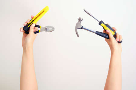 Construction tools at arm's length. Hammer, screwdriver, pliers, paper knife in women's hands outstretchedの写真素材