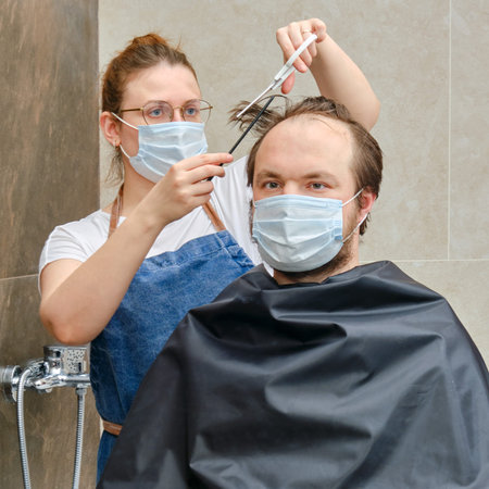 A woman gives a haircut to a man in medical mask, bathroom close-up. Concept of unkempt appearance...