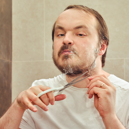 Portrait of a 35-40 year old man, who cuts his beard with scissors, close-up.