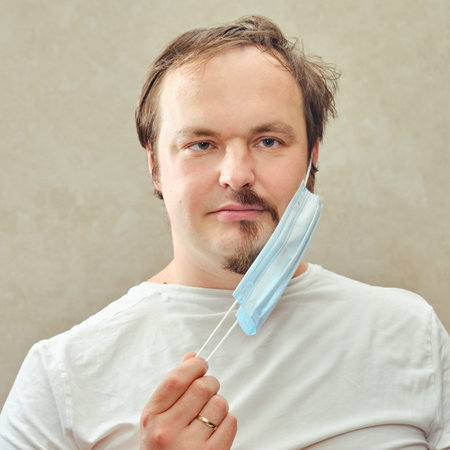 A man takes off a medical mask under which half of his beard is visible. Concept of unkempt...