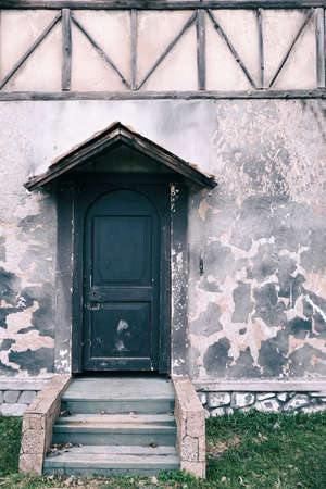 An old wooden door with a porch, steps and a canopy. Wall with dirty paint sprinkled, copy space for text.の写真素材