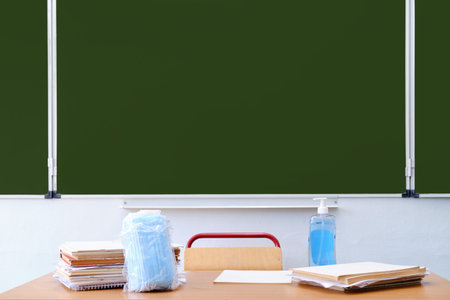 School table with books, sanitizer and medical masks. The blackboard in the classroom during the...