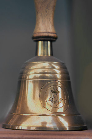 Old ship hand bell made of yellow metal with an anchor pattern, close-up