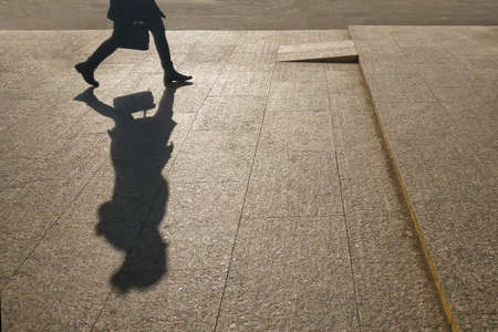 Silhouette of a girl on the background of a city street. A large shadow of a woman walking with a bag. A woman in a hurry on their business.