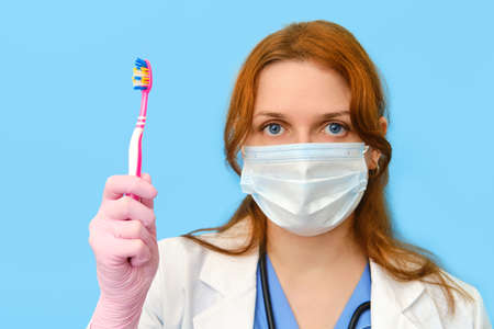 Woman doctor holding a toothbrush on a blue background, close-up.の写真素材