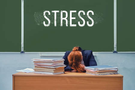 Sad teacher at the school desk at the blackboard with the text "Stress"の写真素材