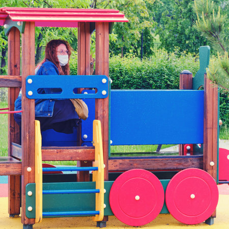 Young woman in a medical mask on a children playground in a toy trainの写真素材