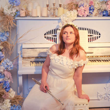 Woman musician sits with a flute on the background of a piano decorated with flowersの写真素材