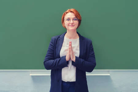 Woman teacher stands at the school blackboard clasped hands in prayer, copy spaceの写真素材
