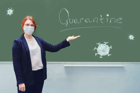School teacher in a medical mask points to a blackboard with the words "Quarantine". Concept problems during isolation due to flu virus.の写真素材