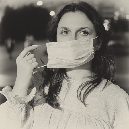 Adult woman removes a medical mask on a night street in the city, black and white