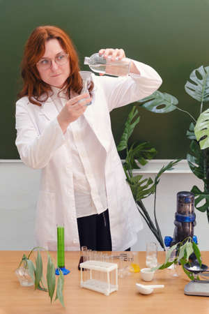 Woman scientist biologist with a bottle of clean water in her hands and test tubes on the table. Chemical research in the educational laboratory of the schoolの写真素材