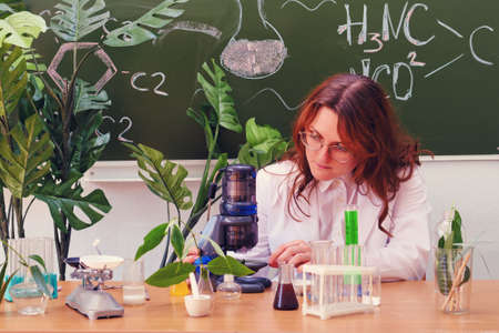 A woman teacher is sitting at her desk with a microscope in her hands. Chemistry lesson in a school class.の写真素材