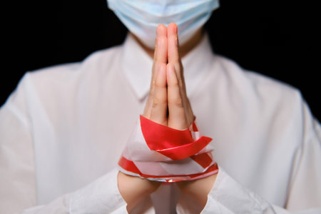 Tied female hands in a person in a medical mask. Portrait of a girl on a black background, the...