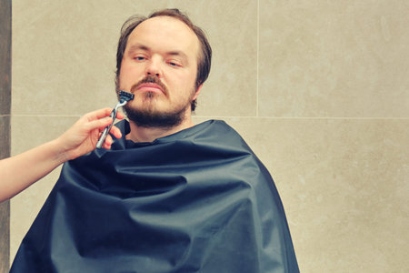 A woman's hand shaves a man's beard with a safety razor, copy spce