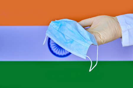 Protective mask in India, concept coronavirus pandemic. Hand in a medical glove holds a mask to protect from the pandemic flu virus among Indian.の写真素材
