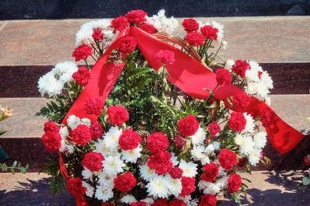 Wreath of flowers with red ribbon, close-up. Funeral wreath of red and white carnations in the cemetery.の写真素材