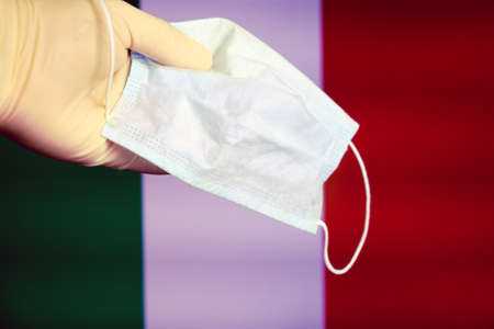 The fight against coronavirus in Italia A hand holds a mask against the background of the Italian flag.の写真素材