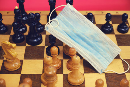 Medical mask on a chessboard with pieces, quarantine closeup