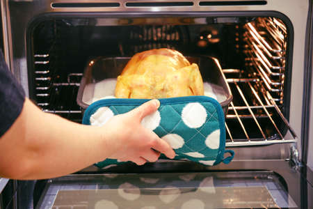 A woman takes a chicken out of the oven with her hand with a potholderの写真素材