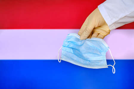 Protective mask in Netherlands, concept coronavirus pandemic. Hand in a medical glove holds a mask to protect from the pandemic flu virus among Dutch.の写真素材