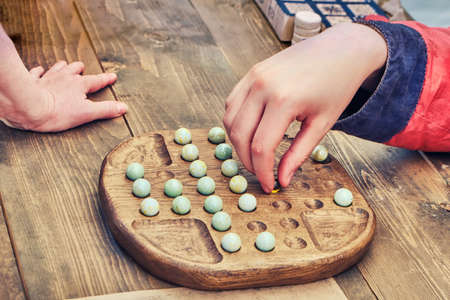 Two people play an ancient board game Mill. Reconstruction of entertainment and leisure in the old days. Vintage intellectual game for two players.の写真素材