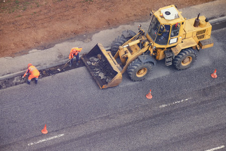 Workers in uniform with a paw remove the asphalt from the road and stacking it in a excavator...