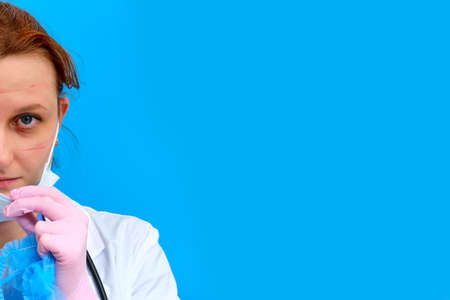 The doctor removes the medical mask after working in the clinic, blue background. Nurse with red eyes in a white coat, copy space for text. Concept stay home because of a virus epidemicの写真素材