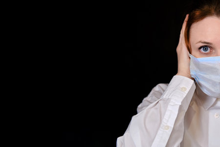 Frightened look of a woman in a protective medical mask on a black background. Concept of people who...