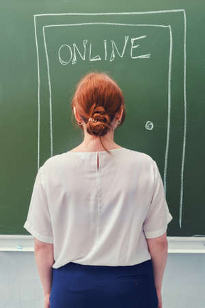 Teacher at the door with the text Online drawn in chalk on a blackboard. Concept of online education at school.の写真素材