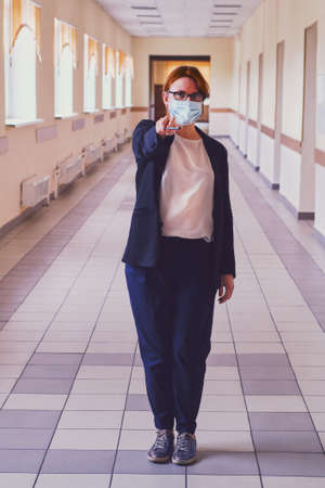 Female teacher in face mask stands in an empty school corridor. Coronavirus quarantine conceptの写真素材