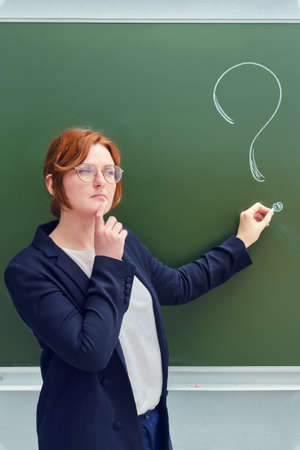 Woman teacher with a sad face and a question mark on a blackboard. Upset school teacher on blackboard backgroundの写真素材