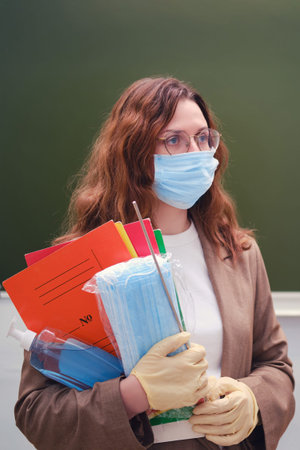 Student woman in a face mask with sanitizer stands at a blackboard