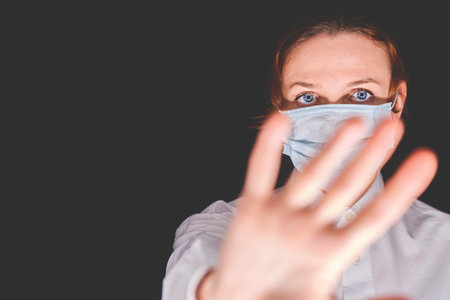 Young woman in medical mask showing stop gesture with hand, copy space. Face girl in a white shirt...