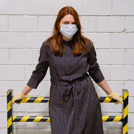 A protective barrier against a white wall and a girl with red hair in a medical mask. Concept of the fight of doctors against diseases and influenza virusesの写真素材