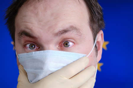 A man in a medical mask with red eyes on the blue backgroundの写真素材