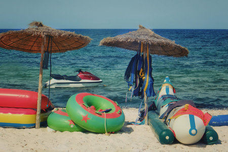 Inflatable circle, mattress and banana under umbrella on sand beach. Bad weather and water rides do...