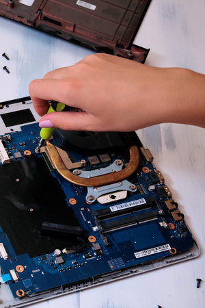 Disassembling the laptop with a female hand on the table with a screwdriver