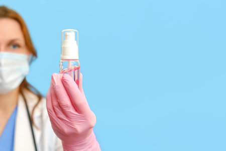 Doctor in a white uniform with a sanitizer in hand on a blue background, copy space.