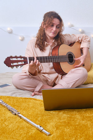 Woman learns music lifestyle. Woman plays the guitar while sitting on yellow bed
